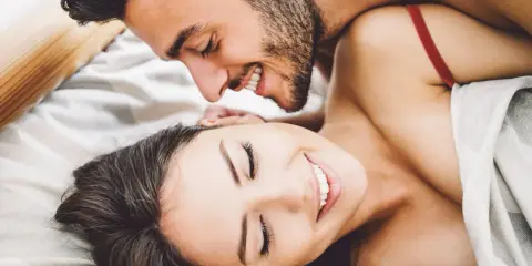 Pareja sonriente en la cama, disfrutando de intimidad.