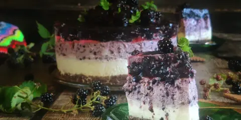 Sernik z jeżynami, warstwowy deser z owocami leśnymi i bitą śmietaną, ozdobiony świeżymi jeżynami i miętą.