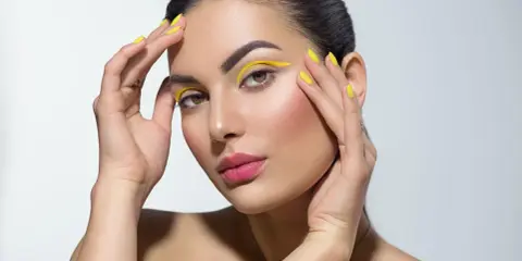 Mujer con un atrevido doble eyeliner amarillo y uñas a juego.