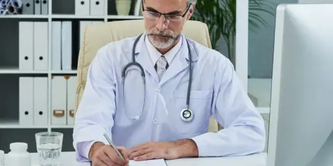 Lekarz w białym kitlu pisze na kartce, zastanawiając się, czy psycholog może wystawić L4.