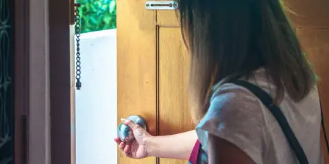 Mano che apre una porta, esitante, con l'ansia di uscire di casa che si fa sentire.
