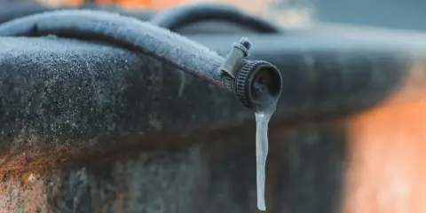 Un tuyau de jardin givré, avec une stalactite de glace tombant du robinet, illustre la nécessité de la protection tuyau en hiver.