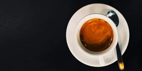 Eine Tasse Espresso mit Crema auf einer Untertasse, daneben eine kleine Löffel. Das perfekte Wasser zum Espresso.