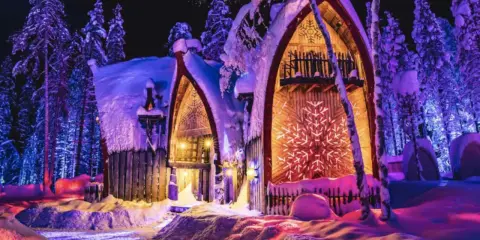 Noche mágica en Finlandia con niños. Casas nevadas iluminadas con luces de colores, rodeadas de árboles cubiertos de nieve.