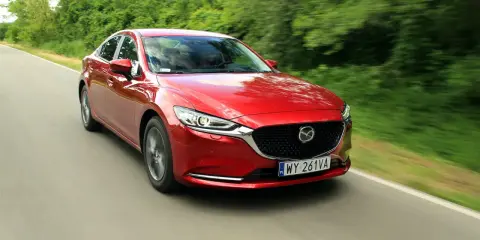 Czerwona Mazda 6 2.0 benzyna pędzi po wiejskiej drodze, otoczona zielenią drzew.