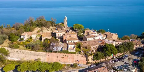 Borgo antico con campanile affacciato sul mare Adriatico. Il centro storico del lungomare Gabicce Mare, con tetti rossi e vegetazione rigogliosa, si estende verso l'azzurro intenso dell'acqua.