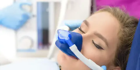 Pacjentka u dentysty z maską do podawania gazu rozweselającego. Zabieg przebiega komfortowo.