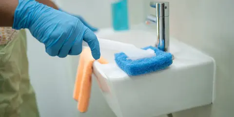 Rękawiczka i gąbka do czyszczenia umywalki ceramicznej. Pomarańczowa ściereczka czeka obok.