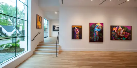 Vibrant artworks adorn the walls of Jackson Fine Art Atlanta, with a large window offering a glimpse of the lush greenery outside.