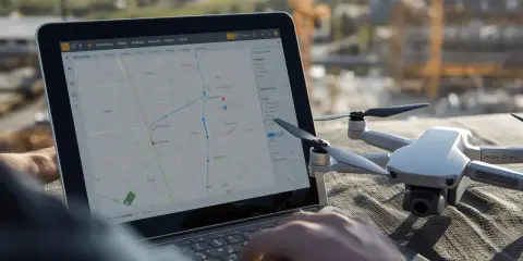 Planowanie zgłoszenie lotu dronem na mapie na laptopie. Obok leży dron.