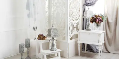 Delikatny salon w stylu shabby chic. Białe meble, ażurowa parawan, świeże kwiaty i ozdobne latarenki tworzą romantyczny nastrój.