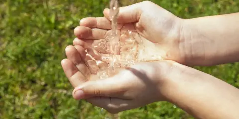 Mains d'enfant recevant un filet d'eau, une façon simple de rendre l'eau moins calcaire pour un usage quotidien.