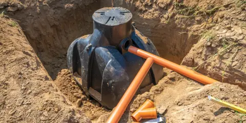 Instalacja szamba w wykopie. Pomarańczowe rury drenarskie i przyłącza czekają na montaż. Trwa praca nad tym, na jakiej głębokości drenaż odwadniający będzie skuteczny.