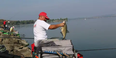 Wędkarz z dumą prezentuje złowioną rybę, obok stoi pojemnik z zanętą Champion Feed.