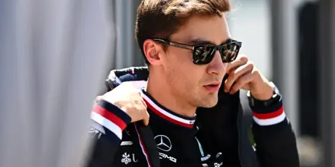 George Russell ajustándose la chaqueta, con gafas de sol y el logo de Mercedes.
