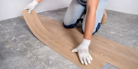 Manos enguantadas colocando suelo vinílico imitación madera sobre suelo de cemento.