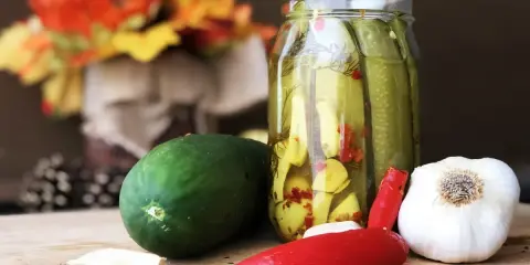 Słoik z ogórkami z chili w plastrach, obok świeży ogórek, czosnek i papryczka chili.