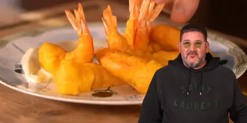 Un hombre sonriente muestra un plato de gambas a la gabardina doradas y crujientes, listas para disfrutar.