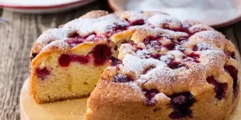 Puszyste ciasto jogurtowe z owocami, posypane cukrem pudrem, wygląda apetycznie. Idealne na deser!