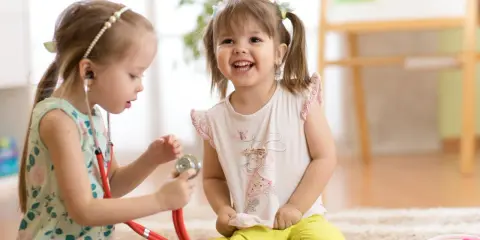 Zwei Mädchen spielen Arzt. Das eine Kind, etwa 7 Jahre alt, untersucht das andere mit einem Stethoskop. Ein spielerischer Einblick in die sexuelle Entwicklung eines Kindes.
