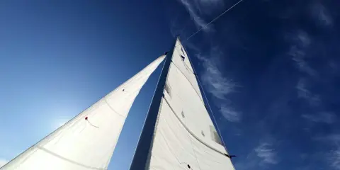 Voiles blanches gonflées par le vent, le bateau semble s'affaler sur l'eau bleue sous un ciel clair.