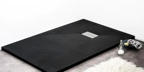 Receveur de douche noir texturé, avec une grille d'évacuation chromée. Un savon et une serviette sont posés sur le bord.
