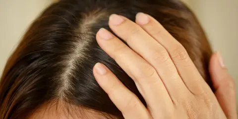 Main d'une femme effleurant son cuir chevelu, peut-être pour vérifier un kyste ou une irritation.