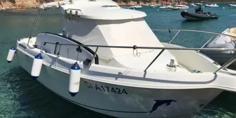 Bateau blanc à quai, avec pare-battages bleus et blancs. Le numéro d'immatriculation est visible, ainsi qu'un dauphin peint sur la coque. Fiche technique du Arvor 20.