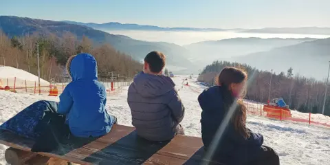Dzieci siedzą na ławce, podziwiając widok na góra żar i dolinę spowitą mgłą.