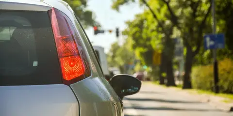 Vista trasera de un coche de autoescuela por dentro, con el piloto rojo encendido. El alumno se prepara para girar.