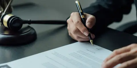 Sądowy młotek i dłoń pisząca dokument. Sprawa dotyczy wydziedziczenia a zachowku.