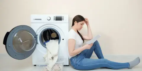 Zmartwiona kobieta szuka w instrukcji, jak zrobić reset pralki Candy.