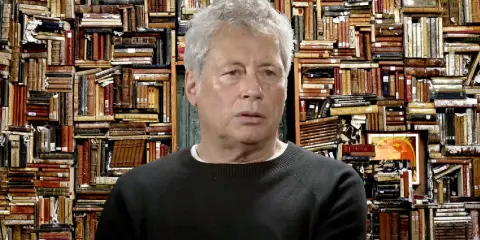 Un uomo con capelli grigi davanti a uno sfondo di libri antichi, forse ispirato ai libri di Alessandro Baricco.