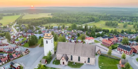 Gammelstad Luleå: en kyrka och ett kluster av röda trähus under en solnedgång.