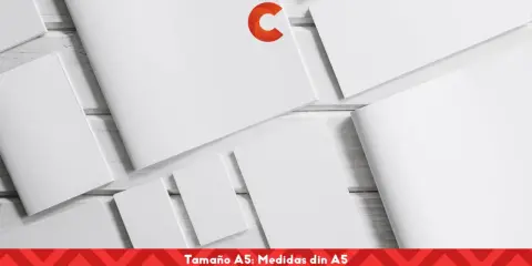 Varias hojas de papel blanco, algunas abiertas y otras cerradas, dispuestas sobre una superficie de madera. Un logo naranja en forma de C destaca en una de las hojas. El texto inferior indica "Tamaño A5: Medidas din A5".