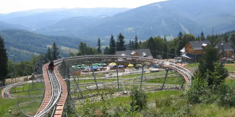 Zjazd kolejką górską w Ustroniu, z widokiem na Beskidy. W tle góry i lasy.
