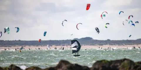 Viele bunte Kites und Surfer bevölkern das Meer am Brouwersdam Zeeland. Ein Kitefoiler schwebt über dem Wasser.
