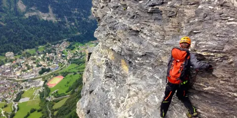 Wspinaczka via ferrata w Szwajcarii. Widok na dolinę i miasteczko z perspektywy skalnej ściany.