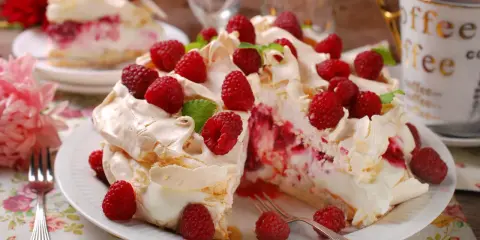 Pyszny tort bezowy z malinami, udekorowany świeżymi owocami i listkami mięty. Idealny na deser.