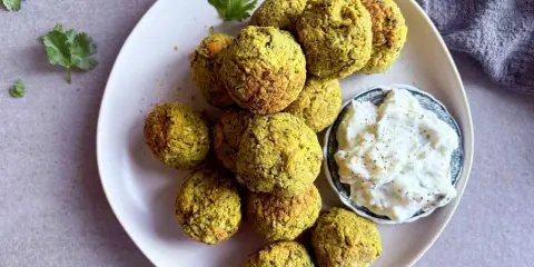 Assiette de falafels dorés, prêts à être dégustés. Une recette facile pour un plaisir garanti. Sauce blanche et coriandre pour accompagner.