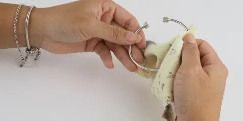 Manos puliendo un brazalete de plata con un paño. Aprende como limpiar cadena de plata y mantener tus joyas brillantes.