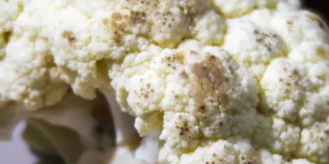 Nahaufnahme eines Blumenkohls mit einigen braunen Stellen, die auf Reife oder leichte Beschädigung hindeuten.