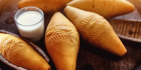 Kilka oscypków z ozdobnymi wzorami i szklanka mleka na drewnianym tle.