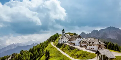 Un borgo incantevole in montagna, perfetto per le tue vacanze in Friuli. Case bianche, una chiesa e sentieri verdi sotto un cielo nuvoloso.