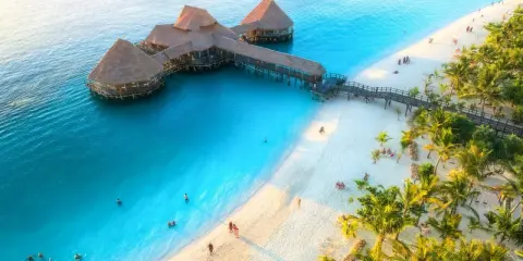 Zanzibar w czerwcu: idealna pogoda na wypoczynek na rajskiej plaży z turkusową wodą i palmami. Widać hotel na wodzie i ludzi kąpiących się.