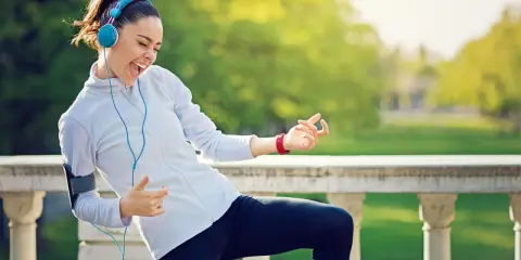 Frau mit Kopfhörern und Handy-Armband spielt Luftgitarre beim Joggen. Die Musik zum Joggen macht sie glücklich.