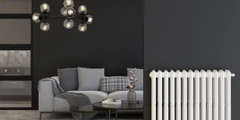 Un salon moderne avec un canapé gris, une table basse et un lustre design. À droite, un radiateur blanc classique, rappelant les anciens panneaux rayonnants.