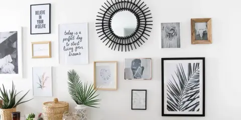 Un mur de cadres éclectique avec un miroir soleil, des photos et des citations inspirantes.