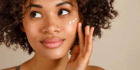 Donna con capelli ricci applica crema sul viso per una pelle bella e luminosa.