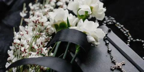Białe kwiaty na pogrzeb, czarna wstęga i różaniec na czarnej tkaninie. Symbol żałoby i pamięci.
